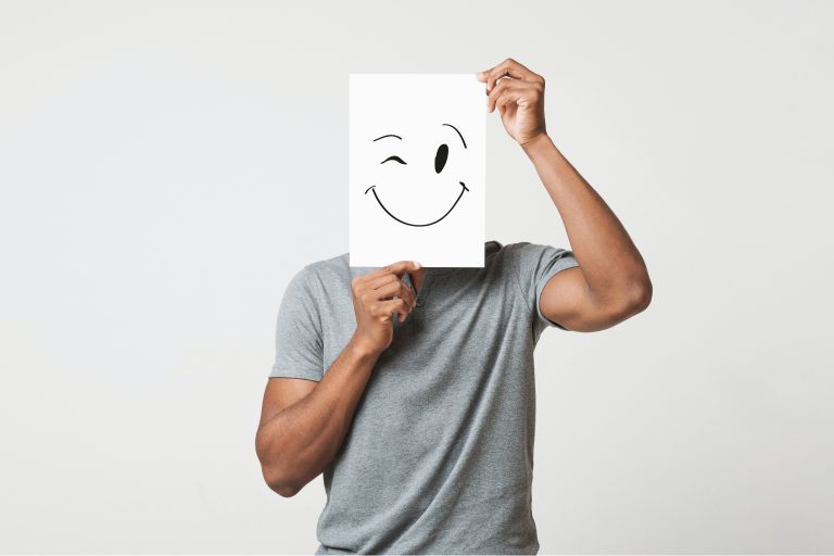 Black man cover his face with happy and winking smiley drawn on paper, white studio background